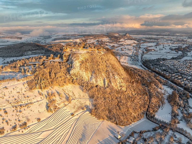 Aerial view of the snow-covered Hegau volcano Hohentwiel with Germany's largest castle ruins on a cold winter morning, at sunrise, in front of it Germany's highest vineyard, the Elisabethenberg at 505 metres above sea level, on the right the town of Singen, on the horizon the neighbouring Hegau volcano Hohenkrähen, district of Constance, Baden-Württemberg, Germany, Europe