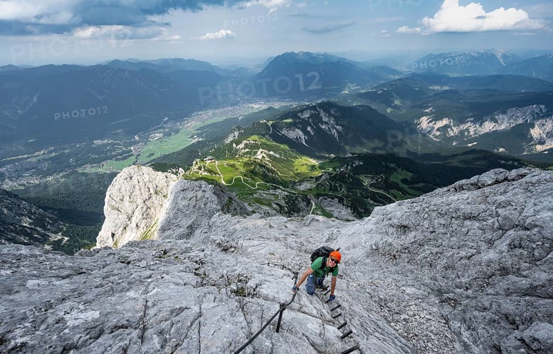 Mountaineer with helmet climbing on the rock in a secured climb, on a narrow rocky ridge, in steep rocky mountain landscape, view of Garmisch Partenkirchen, descent from the Alpsitze via the via ferrata, Alpspitz Ferrata, Wetterstein range, Bavaria, Germany, Europe