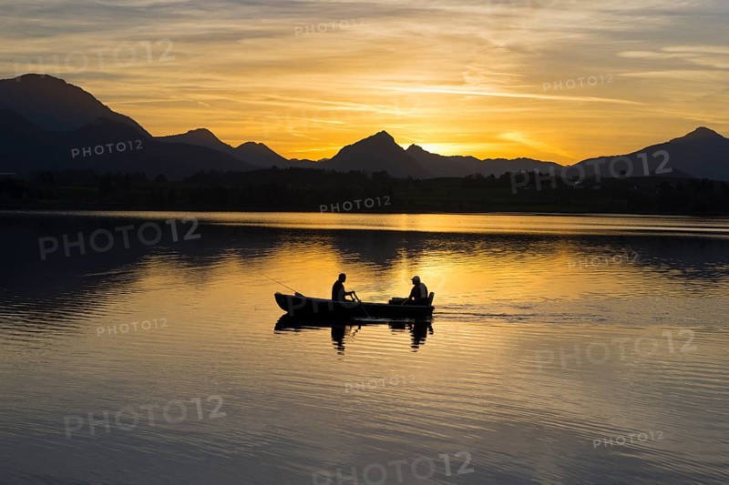 Two people in a boat on a lake at sunset, mountains in the background, Hopfensee, Hopfen am See, Ostallgäu, Allgäu, Swabia, Bavaria, Germany, Europe