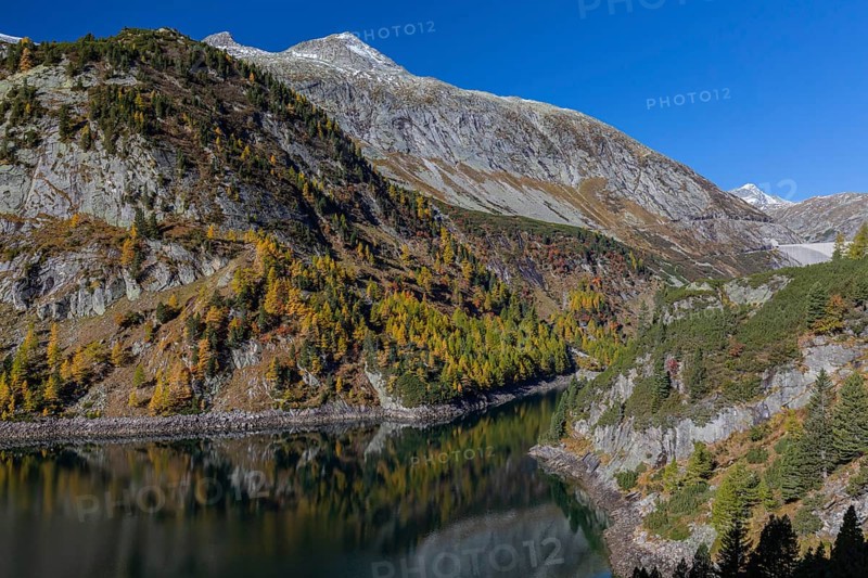 The Galgenbichl reservoir with a mountain forest in fall foliage on a bright sunny morning. Seen from the Malta Hochalm road. Carithia, Austria, Europe