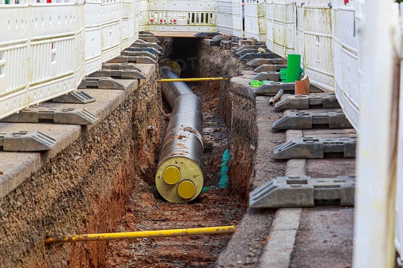 Construction trench with installed district heating pipes and safety fences at a construction site
