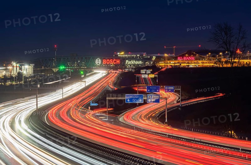 A8 motorway at Stuttgart Airport in the evening. Heavy traffic, lanes of light. Modern architecture of Messe Stuttgart with multi-storey car park above the motorway lanes. Logo of the Bosch company. Stuttgart, Baden-Württemberg, Germany, Europe
