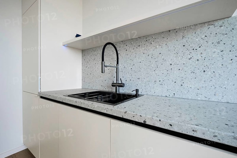 A sleek kitchen area showcases a minimalist design with a modern countertop and stylish black sink. The light-colored cabinetry complements the clean lines and sophisticated aesthetics of the space.
