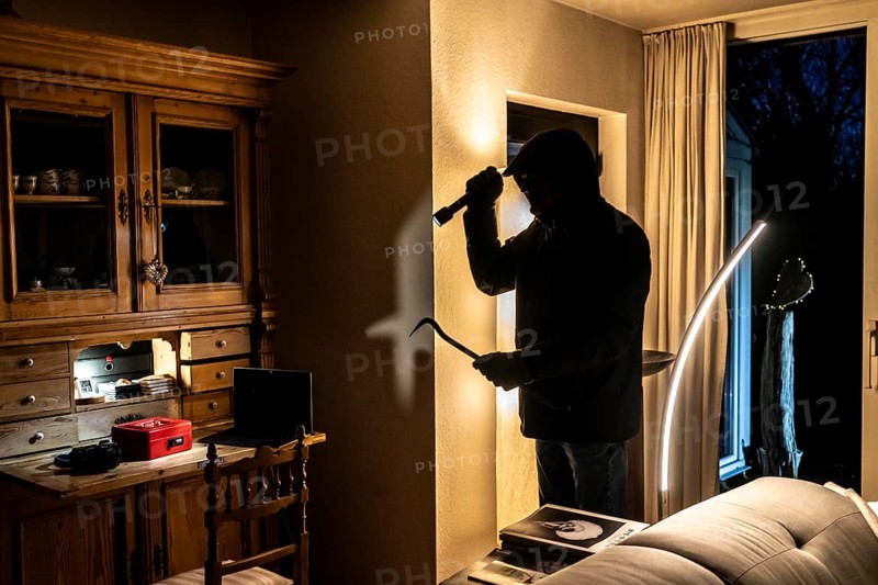 Symbolic image of a burglary, perpetrator has broken into a flat from the garden side and is looking for loot, cash box, valuables, money, technology