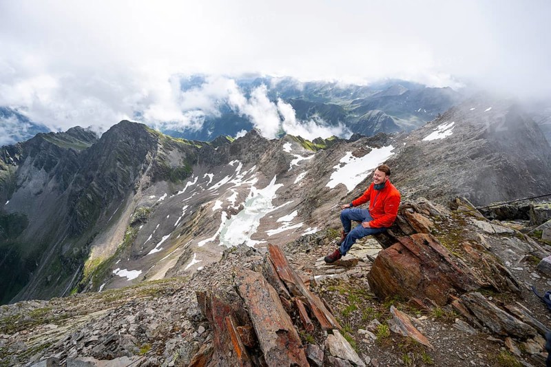 Mountaineer sitting on a rock, cloudy mountain landscape at the summit of Lasörling, view to Berger Kees and mountain peak Schober, Lasörling Group, Hohe Tauern National Park, East Tyrol, Tyrol, Austria, Europe