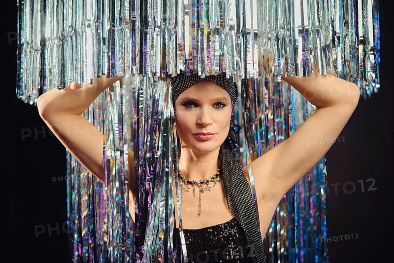 A performer poses confidently with a shimmering headdress made of reflective materials, exuding elegance and style. The vibrant setting enhances her captivating look during a luxurious event
