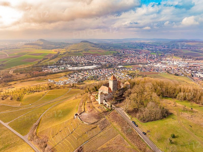 A castle stands above the fields and the village, surrounded by picturesque hills under a cloudy sky, Lichtenberg Castle, Oberstenfeld, Germany, Europe