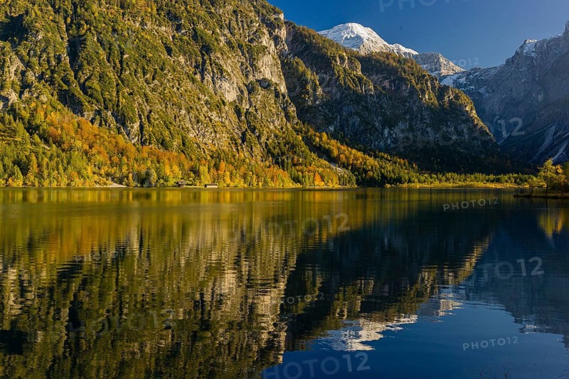 Lake Almsee in autumn with mountains reflected in the lake. Blue sky with no clouds