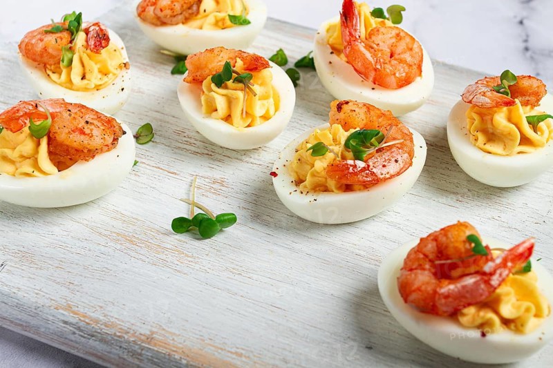 Boiled eggs stuffed with yolk and seasoned with mayonnaise, stuffed eggs with shrimp, on a white wooden chopping board, selective focus, close-up, without people