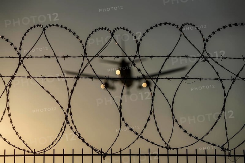 Symbolic image security at the airport, outer fence at Düsseldorf International Airport, steel wire fence, with S-wire rolls, NATO wire, on the top of the fence, aeroplane approaching, sunset, North Rhine-Westphalia, Germany, Europe