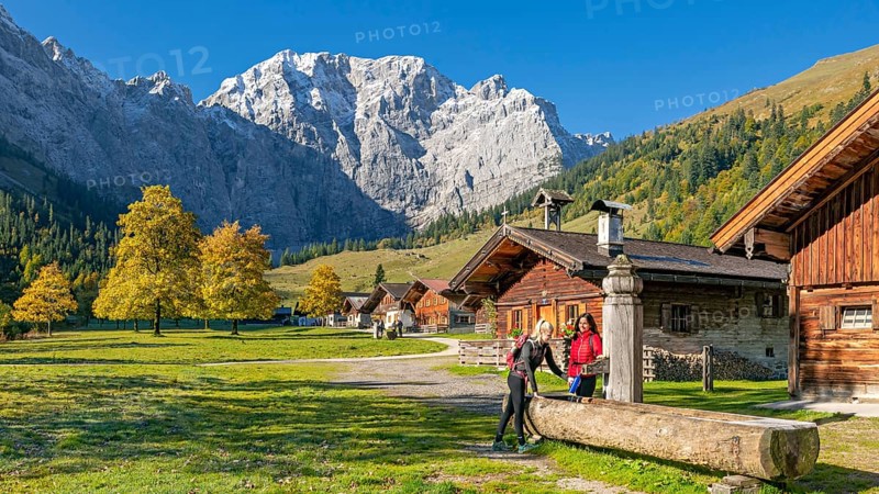 The alpine village of Eng in autumn, two hikers fill a water bottle at the wooden fountain, Eng-Alm, Karwendel Mountains, Tyrol, Austria, Europe