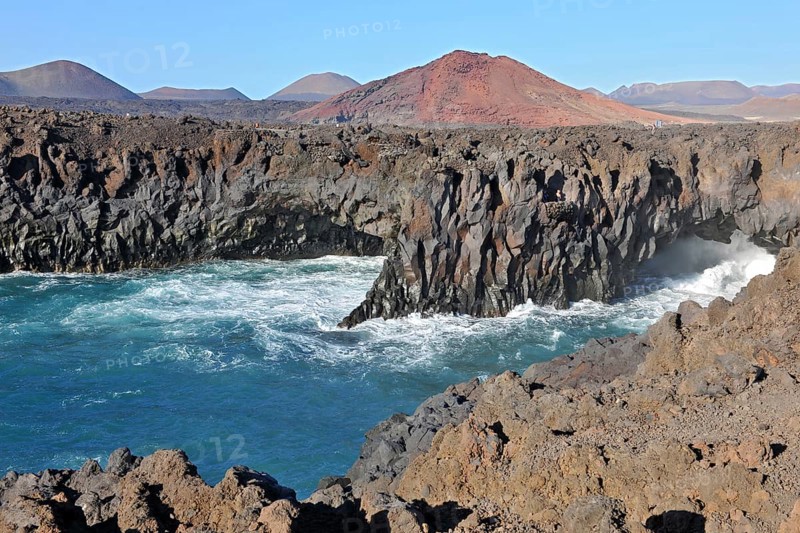 Rugged rocky coastline created by prehistoric volcanic activity Volcanism in early history Bay of lava rock, eroded former volcanoes in the background Volcanic cone, Lanzarote, Canary Islands, Spain, Europe