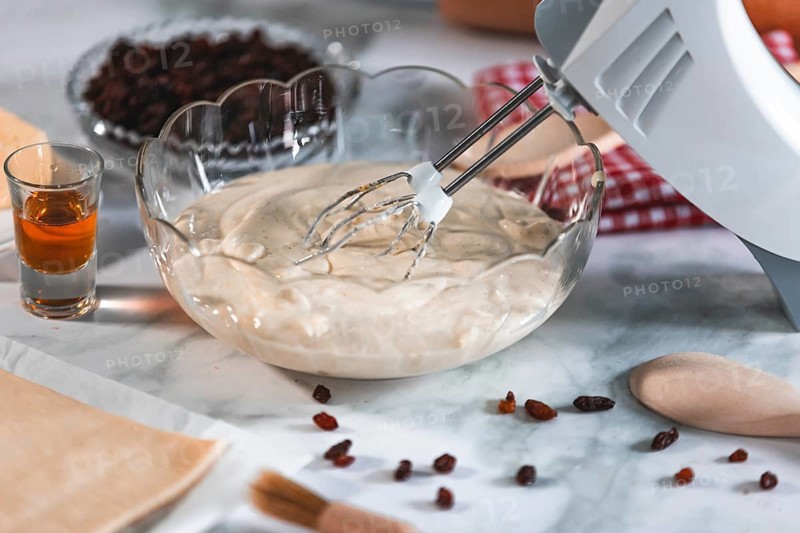 An electric mixer stirs cream of curd cheese, rum and sultanas next to it