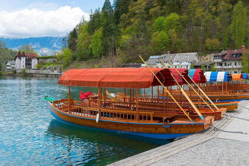 Wooden boat with red canopy on the lake in front of a wooded slope with houses, Lake Bled, Lake Veldes, Blejsko jezero, Bled, Veldes, Feldes, Oberkrain region, Gorenjska, Slovenia, Balkans, Europe