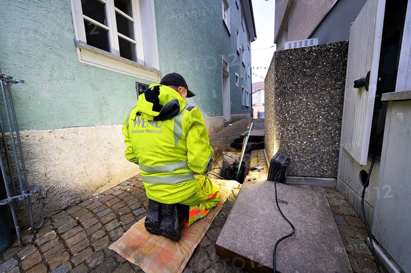 Worker in high-visibility clothing kneeling on cobblestones during construction work next to buildings, Wend Glasfasermontage during the installation of conduits for fibre optic cables, Meßkirch, district of Sigmaringen, Germany, Europe