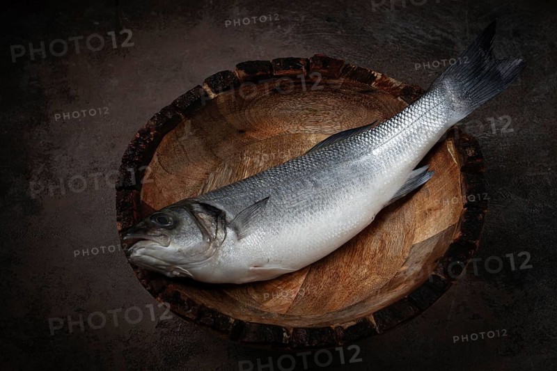 Fresh, raw sea bass fish, in a wooden plate, top view, no people