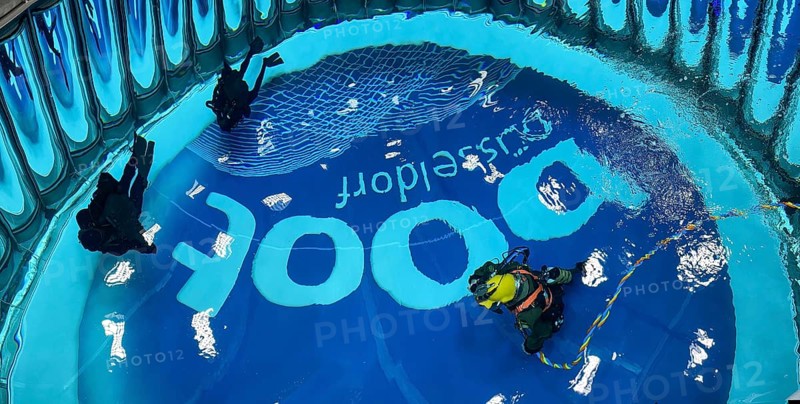 View from above into the diving tower of Messe boot Düsseldorf, on the left recreational diver, on the bottom right helmet diver with hose for air supply from outside the water, on the ground logo and lettering of Messe boot, Düsseldorf, North Rhine-Westphalia, Germany, Europe