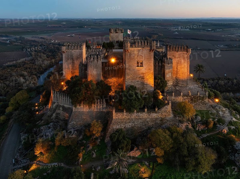 The impressive eighth-century Moorish castle of Almodóvar del Río perches high above the Guadalquivir river valley. Floodlit at dusk. Aerial view. Drone shot. Córdoba province, Andalusia, Spain, Europe