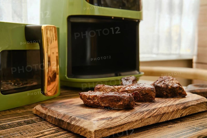 Juicy pieces of meat rest on a wooden cutting board after being fried in modern air fryer