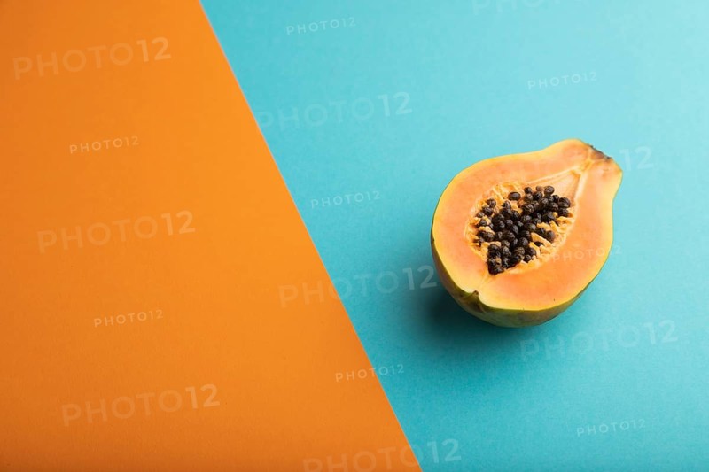 Ripe cut papaya on orange and blue pastel background. Side view, copy space. Tropical, healthy food, women health concept, minimalism