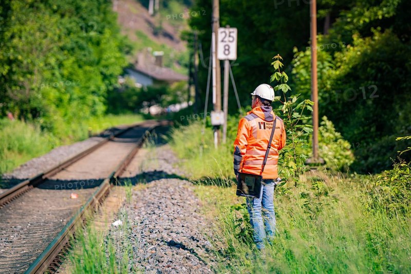 A worker in protective clothing and helmet stands next to railway tracks, surrounded by nature and green foliage in sunny weather, bridge lifting Hermann Hesse Bahn, Calw, Germany, Europe