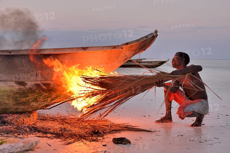 Fisherman smoking his boat with burning palm fronds, to harden the surface and to remove vermin, Dongwe Beach, Dongwe, Zanzibar, Tanzania, Africa