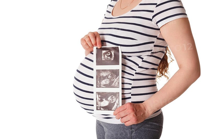 Pregnant woman standing and holding her ultrasound baby scan picture isolated on white