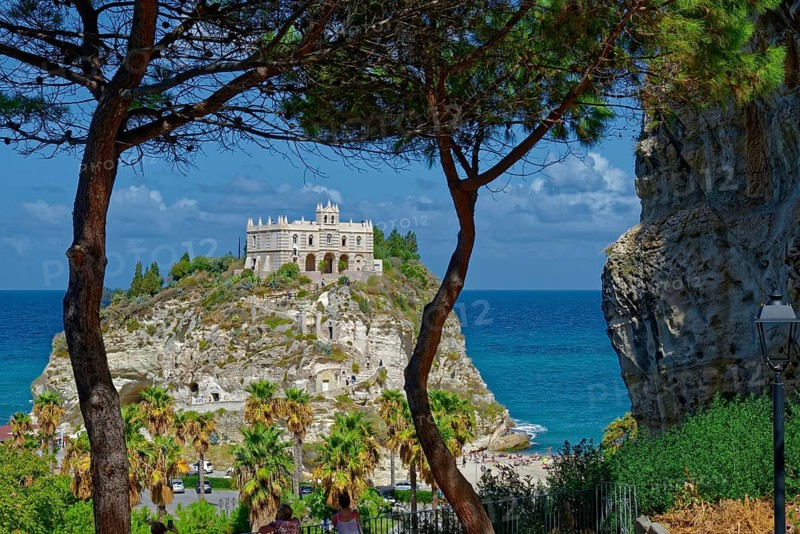 View through pine trees to the medieval church Santuario di Santa Maria dell Isola di Tropea built on rocks of sandstone with turquoise sea, Tropea, Calabria, Vibo Valentia, Southern Italy, Italy, Europe