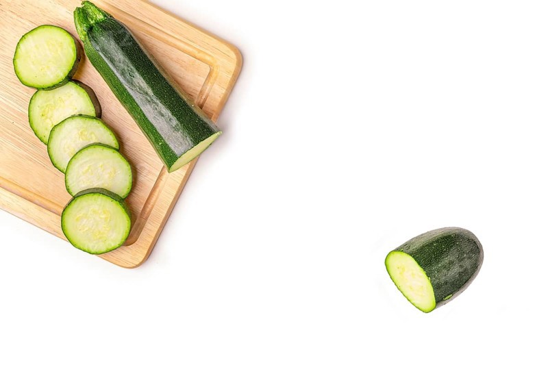 Courgettes (Cucurbita pepo), cut open, on wooden board, on white, copy room