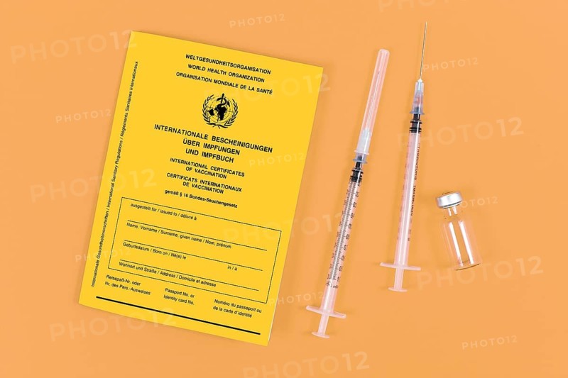 Vaccine concept with syringes, vial and yellow international certificate of vaccination on orange background