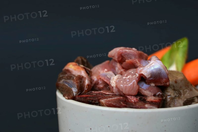 Dog bowl filled with mixture of biologically appropriate raw food containing of meat chunks with fat and healthy vegetables on black background