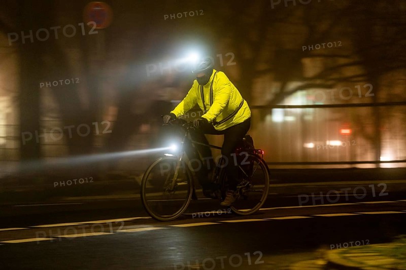 Cyclist with 2 lights and yellow cycling jacket, luminous, inner city traffic, fog, autumn, winter, evening rush hour traffic