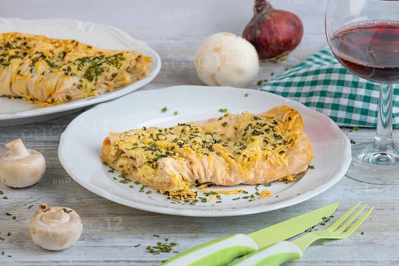 Savoury strudel with cheese and ham on a plate, alongside cutlery and a glass of red wine