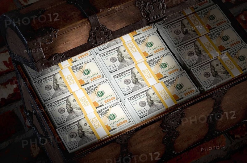 Flashlight shining on a treasure chest filled with millions of dollars in cash in a dark room