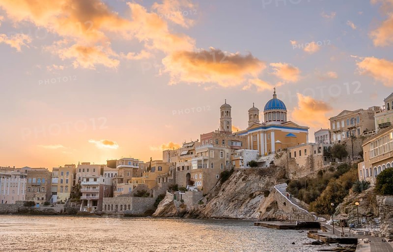 View of the village with the Greek Orthodox church of Agios Nikolaos, Asteria Beach, at sunset with atmospheric clouds, Ermoupoli, Syros, Cyclades, Greece, Europe