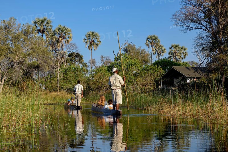 Tourists in a mokoro or dugout boat on safari in swamp area, Gomoti Plains Camp, Gomoti Concession Area, Okavango Delta, Botswana, Africa