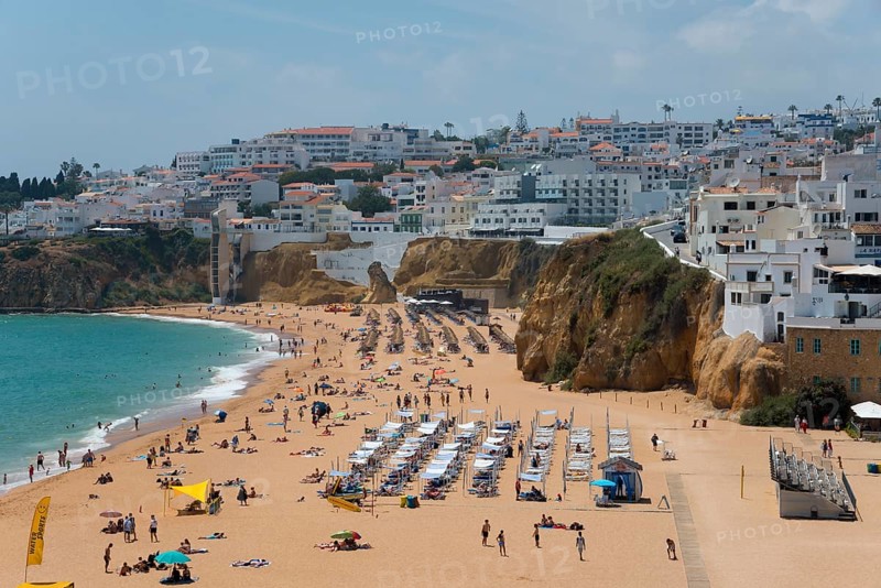 Lively sandy beach with lots of people and sun loungers in front of picturesque cliffs and a coastal town, Albufeira, Faro, Algarve, Portugal, Europe