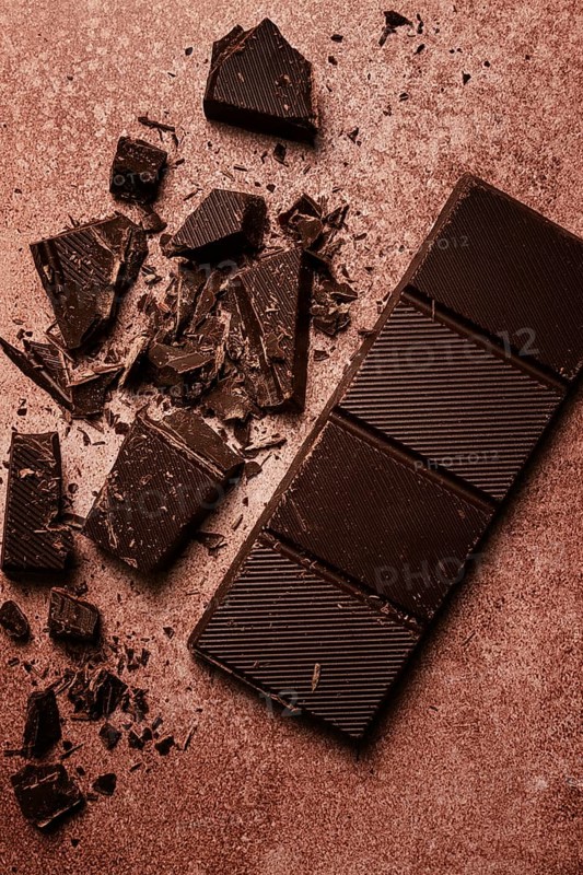 Chocolate bar, for the manufacture of confectionery, broken, crumbled, on a brown background, top view