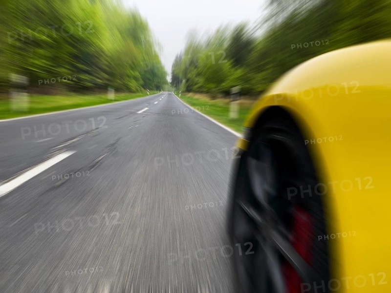 Photo with low camera perspective of car speeding at high speed without speed limit on country road through forest, Germany, Europe
