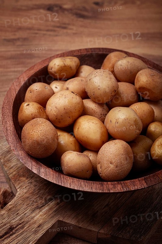 Small, unpeeled potatoes gathered together in a rustic wooden bowl, highlighting their earthy texture and natural colors against a warm wooden backdrop.