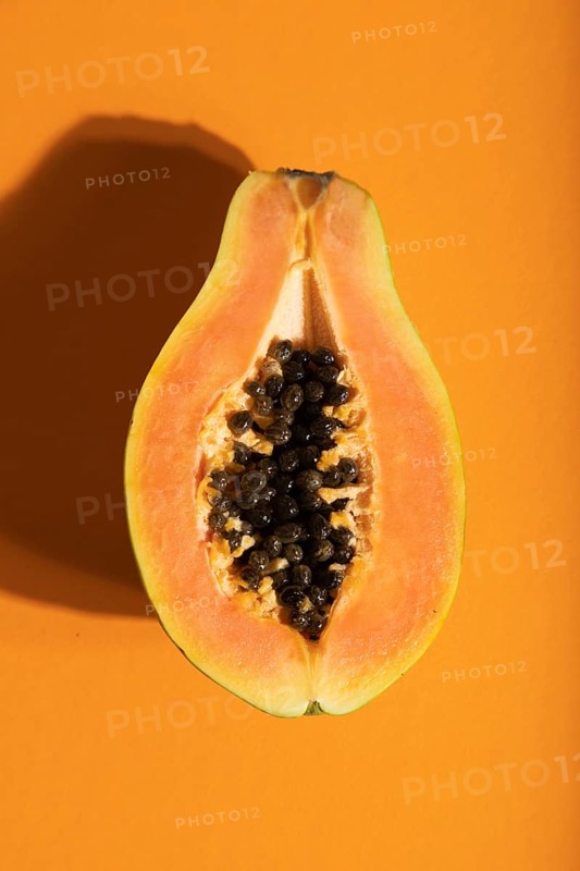 Ripe cut papaya on orange pastel background. Top view, flat lay, close up, hard light. Tropical, healthy food, women health concept, minimalism