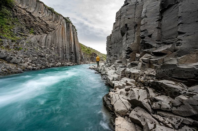 Tourist standing by the river in Stuðlagil Canyon, turquoise blue river between basalt columns, Egilsstadir, Iceland, Europe