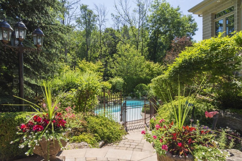 In-ground swimming pool surrounded by copper coloured wrought iron metal security fence and various perennial plants, shrubs and trees in backyard of luxurious home, Quebec, Canada, North America