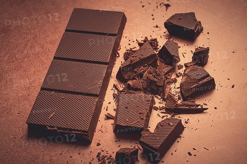 Chocolate bar, for the manufacture of confectionery, broken, crumbled, on a brown background, top view