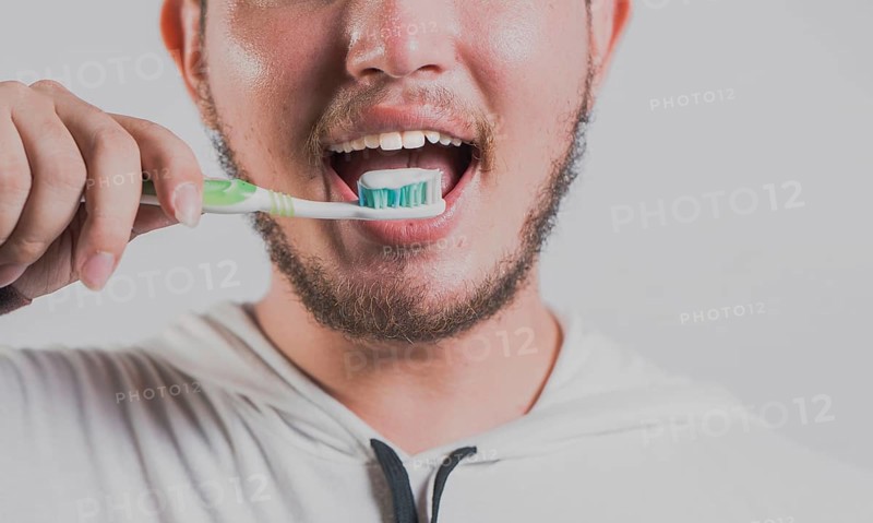 Health and tooth brushing concept. Smiling man brushing teeth isolated