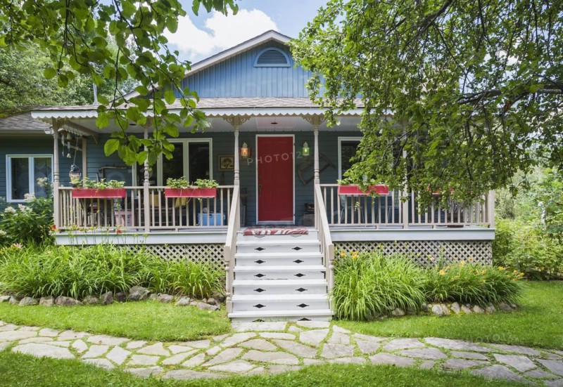 Blue and tan country cottage style residential home facade with veranda in summer, Quebec, Canada, North America