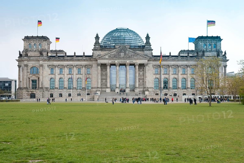 The Reichstag building in Berlin with visitors in front of it, German flags, European flag, flags, green lawn with some trees in spring, windy day, Berlin, Germany, Europe