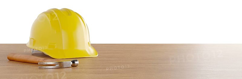 Yellow construction hard hat and hammer resting on wood surface banner isolated on a white background