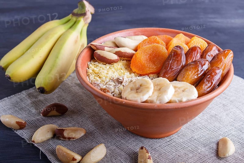 A plate with muesli, banana, dried apricots, dates, Brazil nuts on a black wooden background. close up. copy space