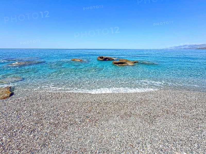 Fine pebble beach with small pebbles stones behind turquoise blue sea sea water calm sea bathing bay without waves in bay Gulf of Messara on Libyan Sea Mediterranean, Crete, Greece, Europe
